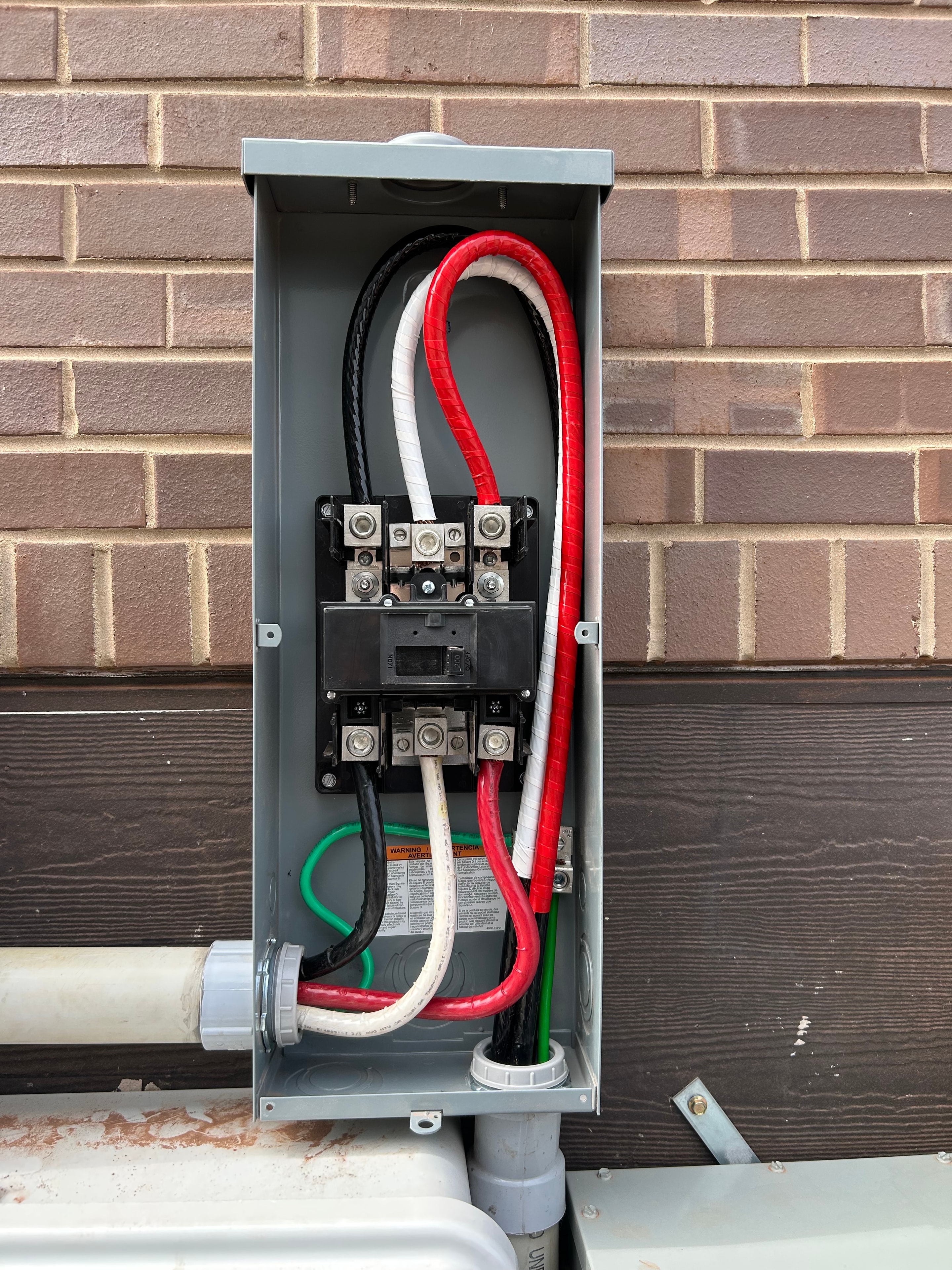 200 amp service disconnect with red and black service entrance wiring on brick exterior