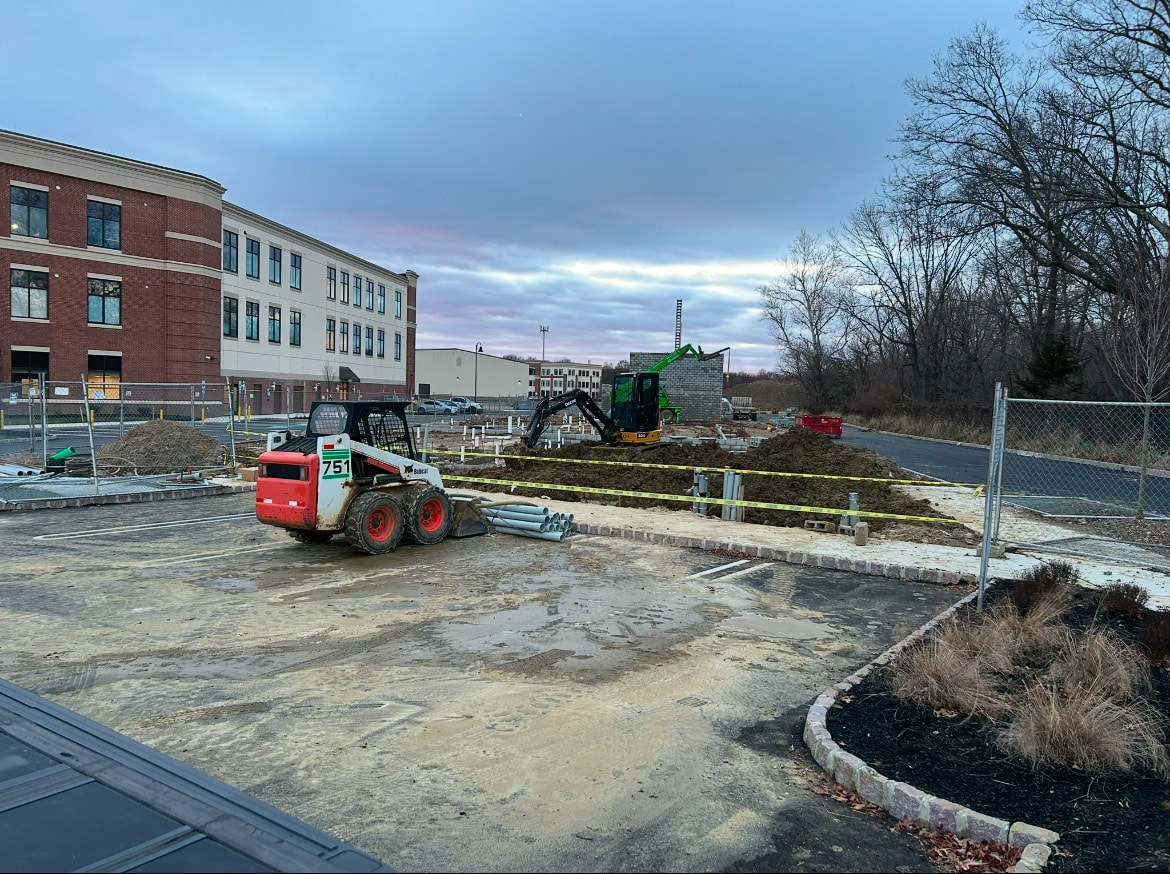 Bobcat skid steer and excavator working underground conduit installation at apartment building construction site