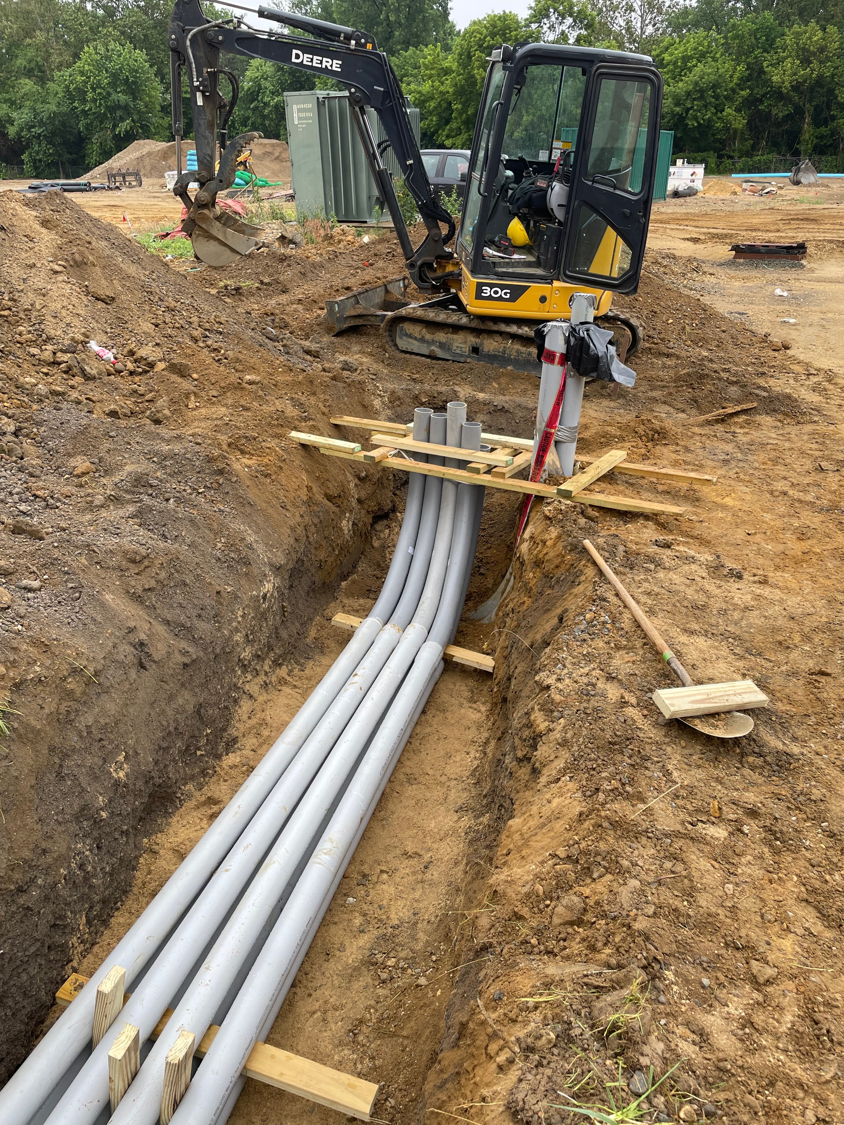 John Deere 30G mini excavator with PVC conduit bundle staged on wooden sleepers in trench