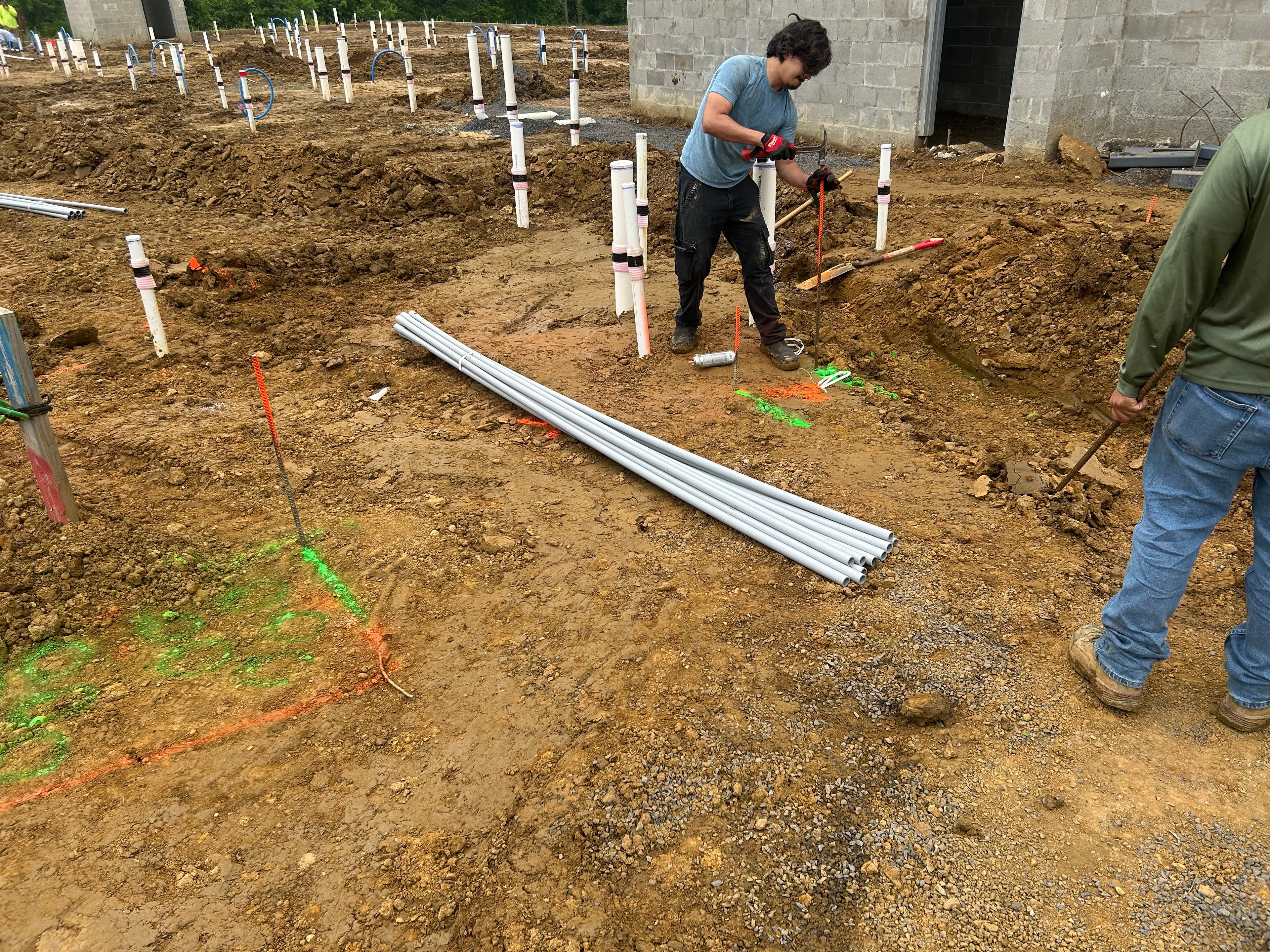 Worker setting PVC conduit stubs with utility locator markings in excavated building foundation area