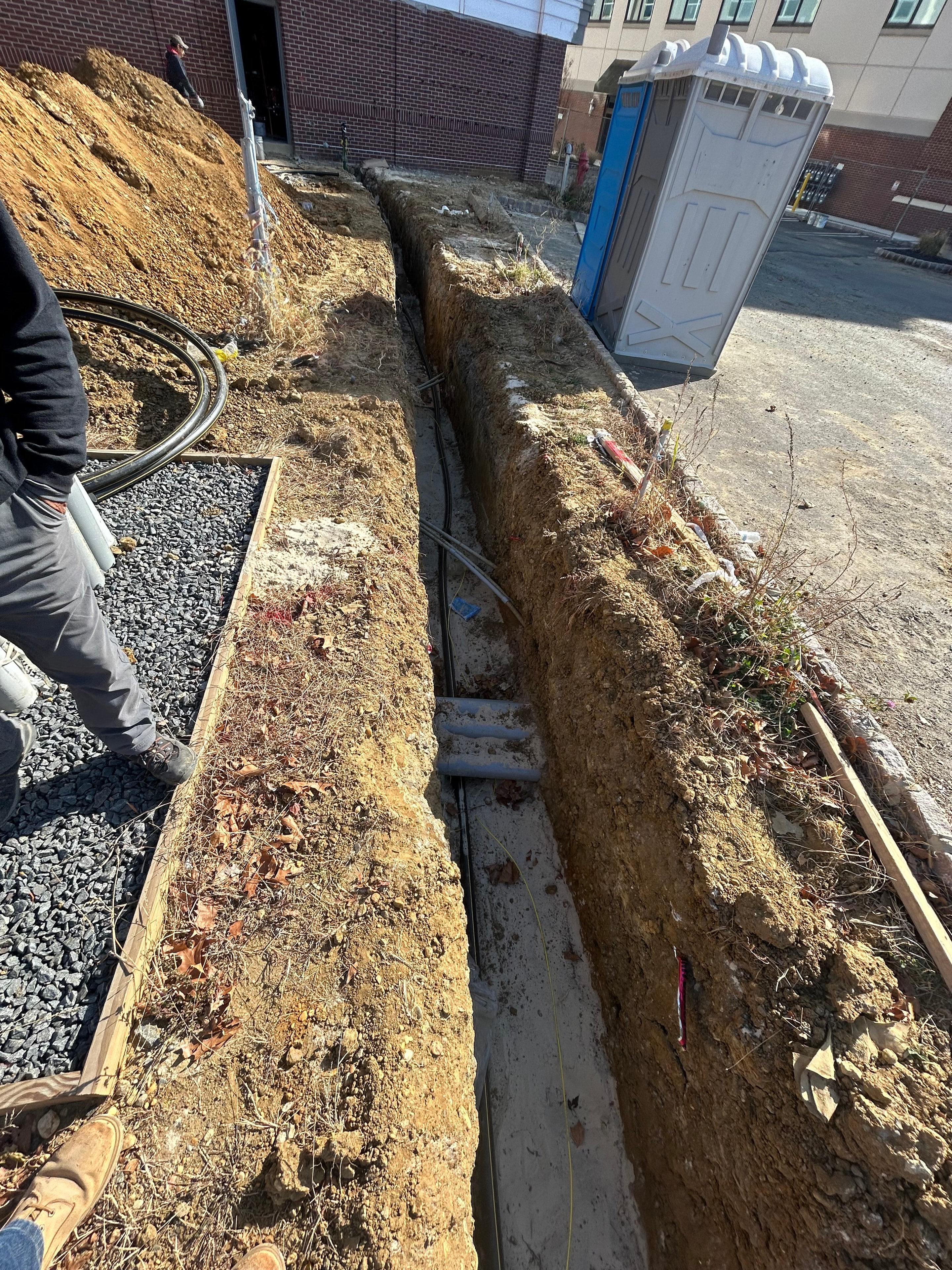 Deep utility trench with PVC conduits entering concrete duct bank alongside existing underground infrastructure