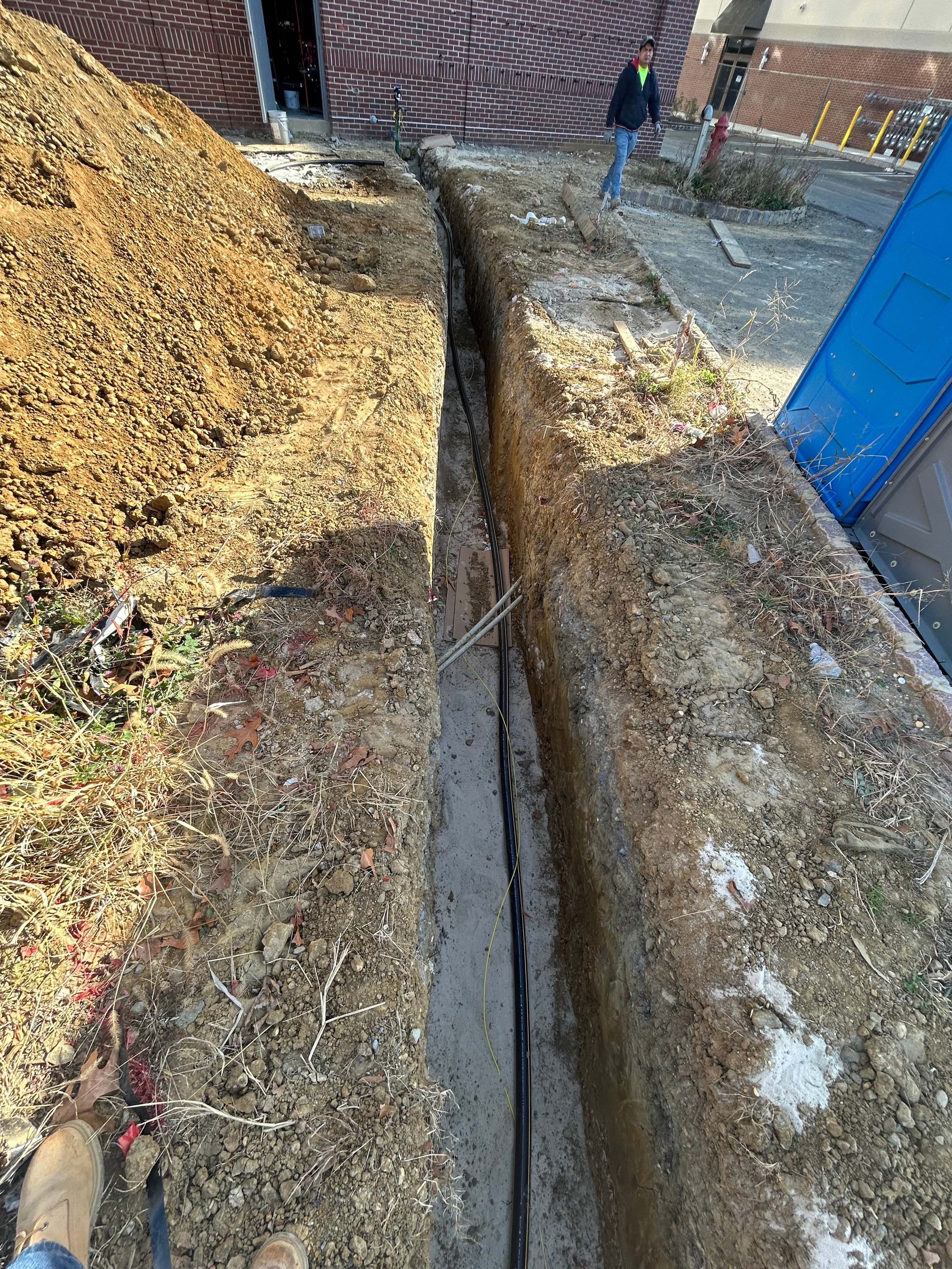 Utility trench with PVC conduit runs and concrete manhole structure at active construction site