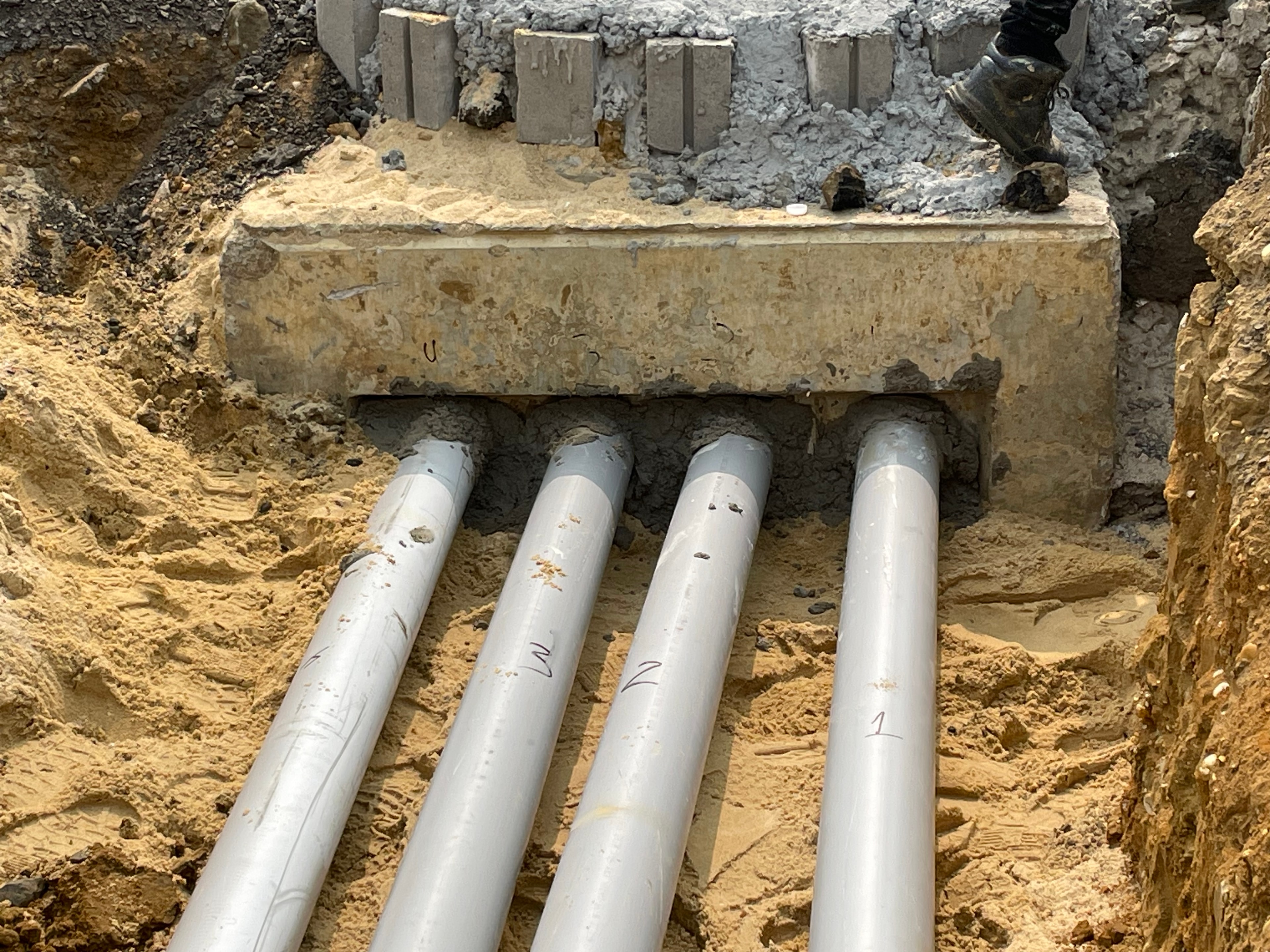 Four numbered PVC primary conduits entering concrete duct bank encasement in sandy trench