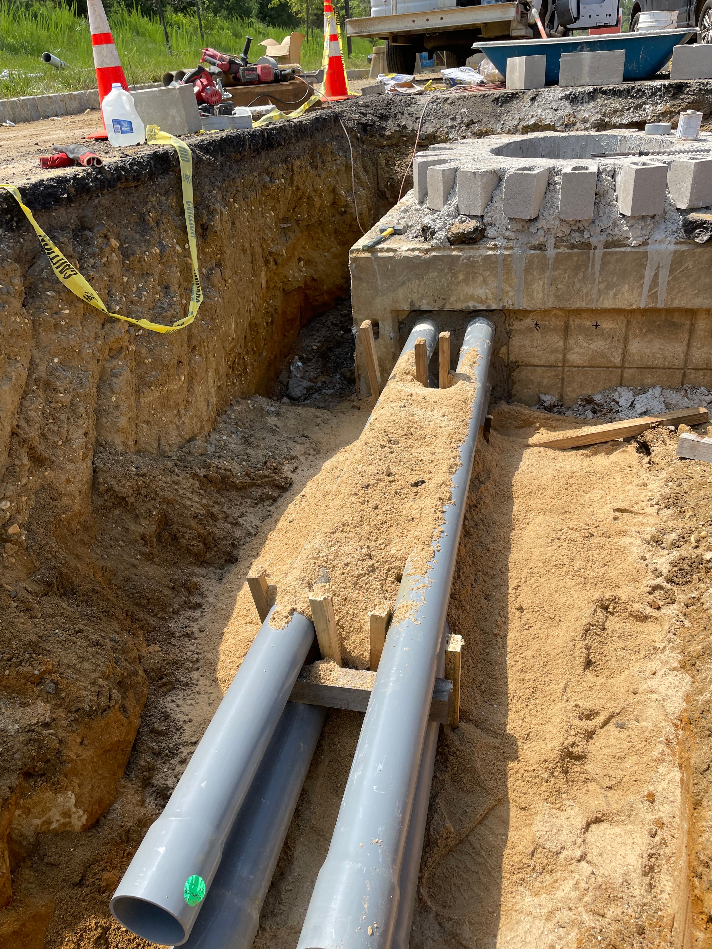 PVC conduit sweeps passing through concrete foundation wall with wooden spacers in deep excavated trench