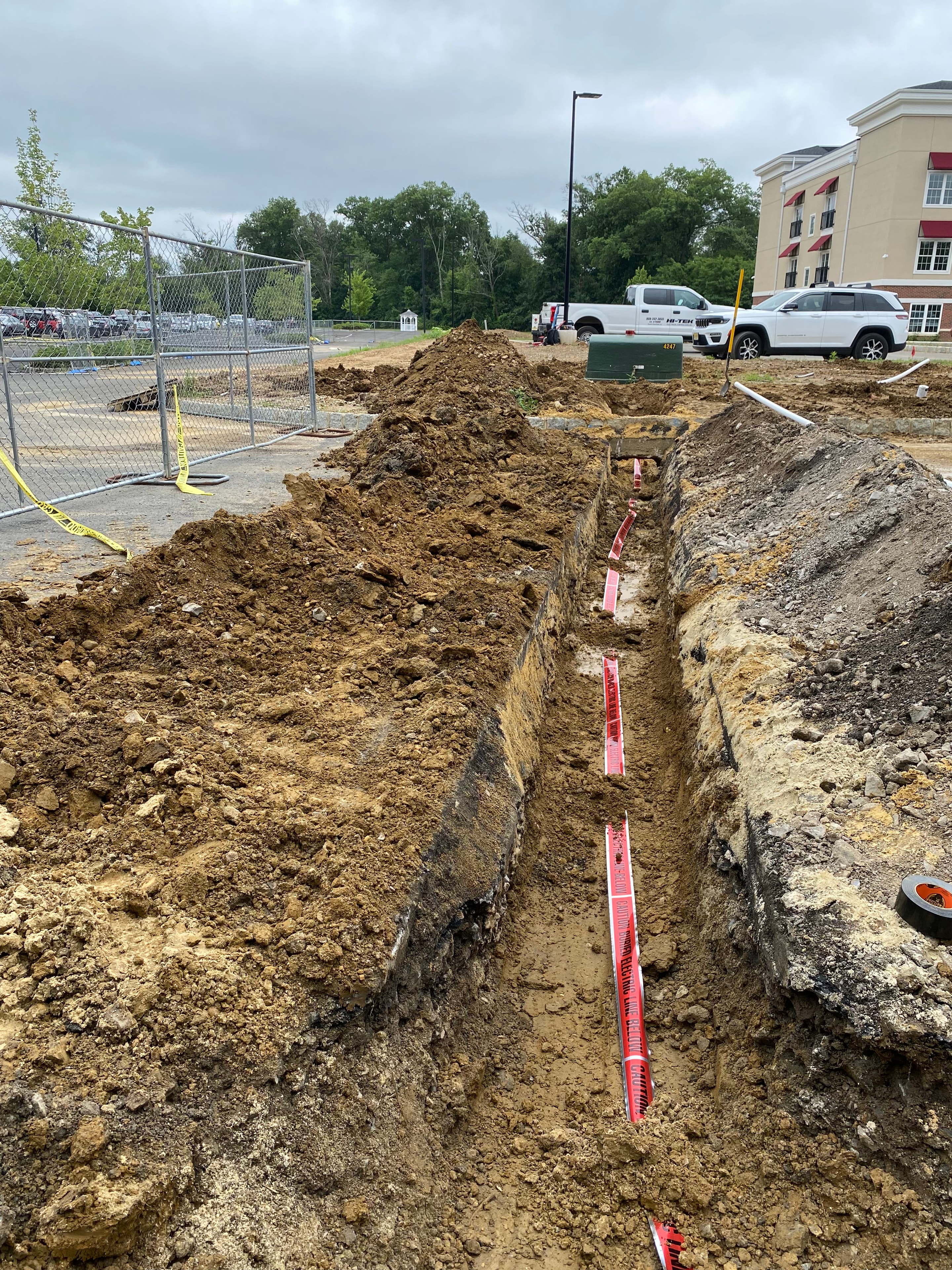 John Deere 30G excavator alongside open trench with "Caution Electric Line Below" tape and single PVC conduit run