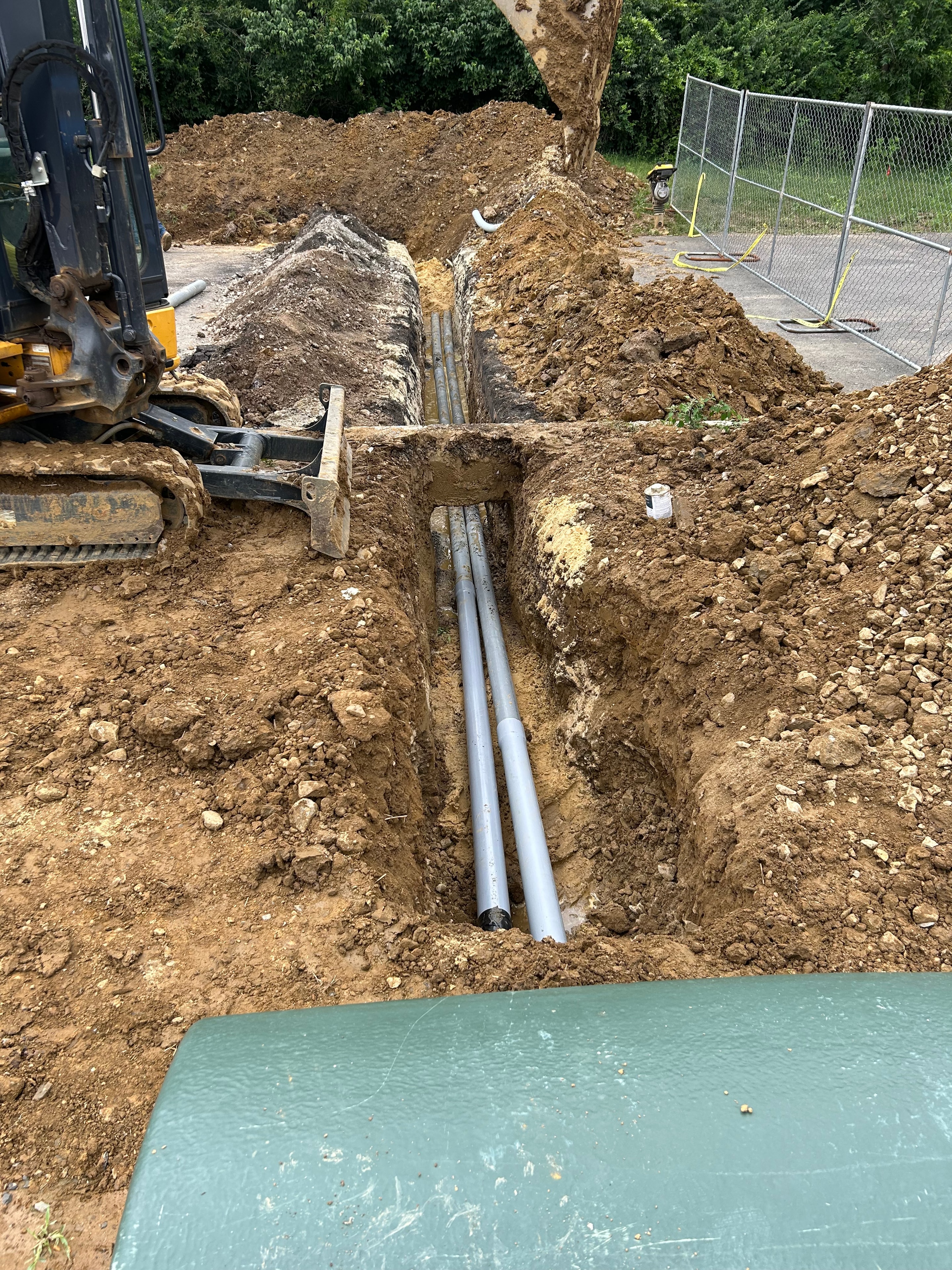 Excavator and crew working on utility primary loop conduit installation at active construction site